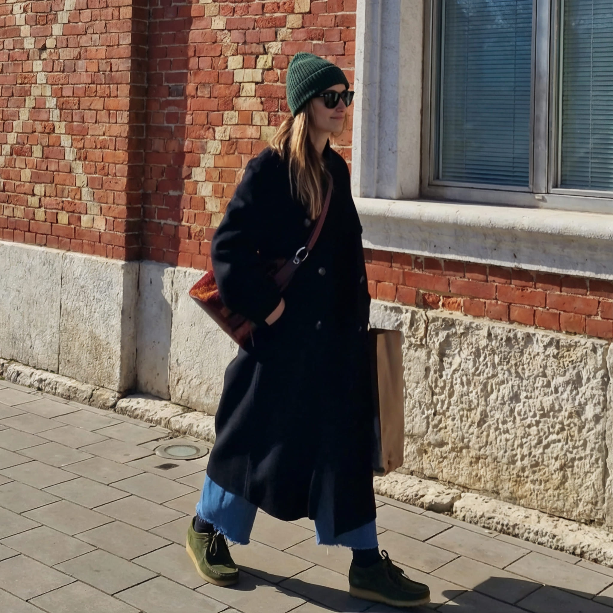 Persona caminando por la calle con abrigo oscuro y pantalón azul, llevando zapatos tipo wallabee negros.