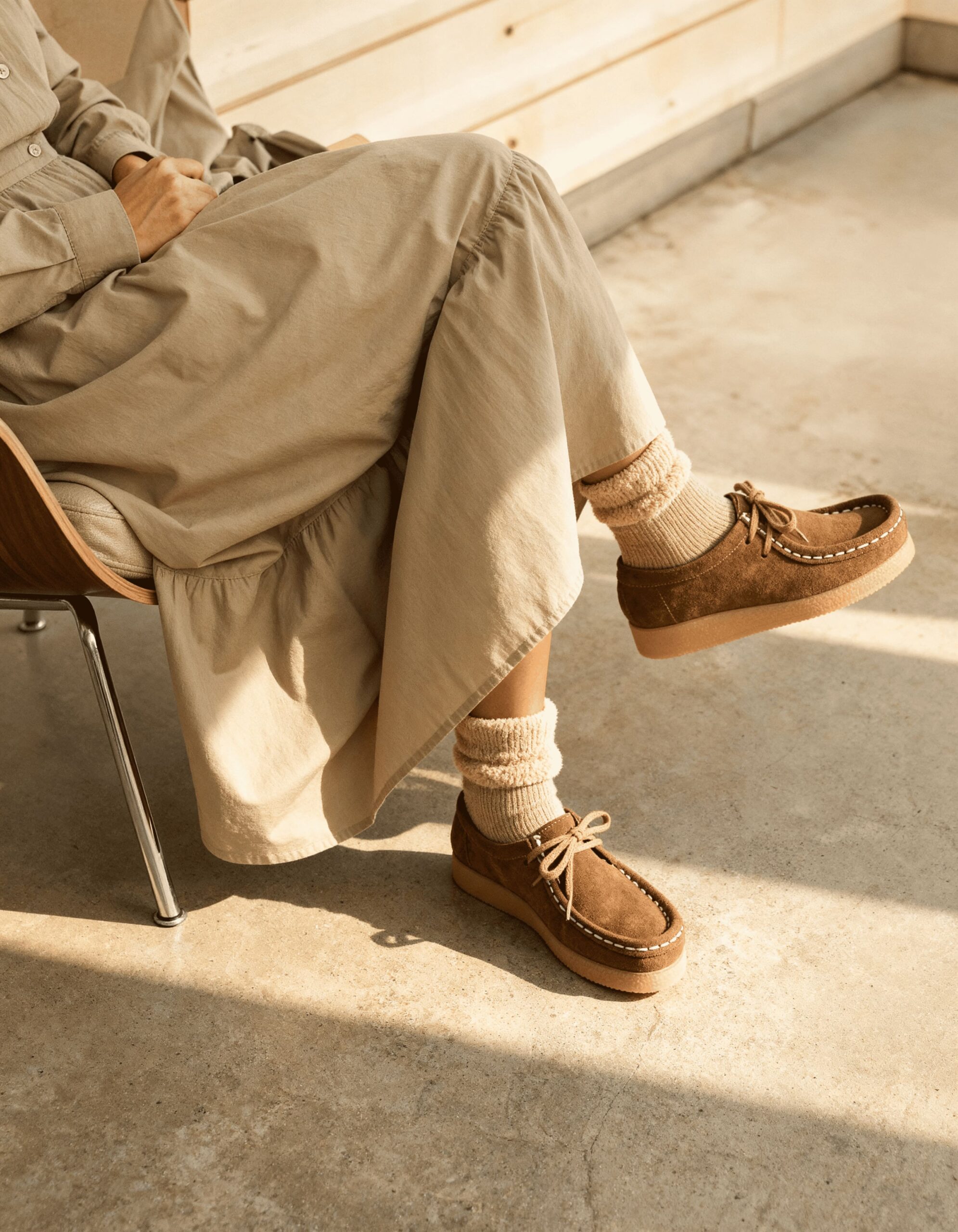 Personne assise portant un pantalon beige et des chaussettes écrues avec des chaussures en daim marron à lacets.